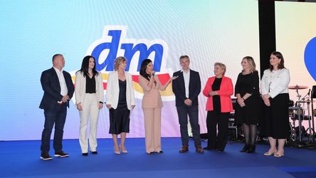Osam članova dm uprave stoji na bini. Jedna osoba drži mikrofon i obraća se publici.