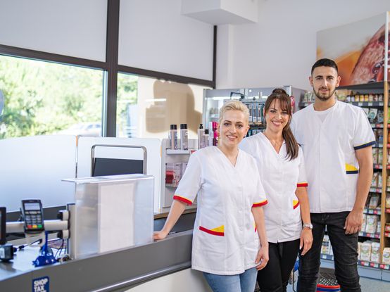 dve koleginice i kolega stoje ispred kase i gledaju u kameru